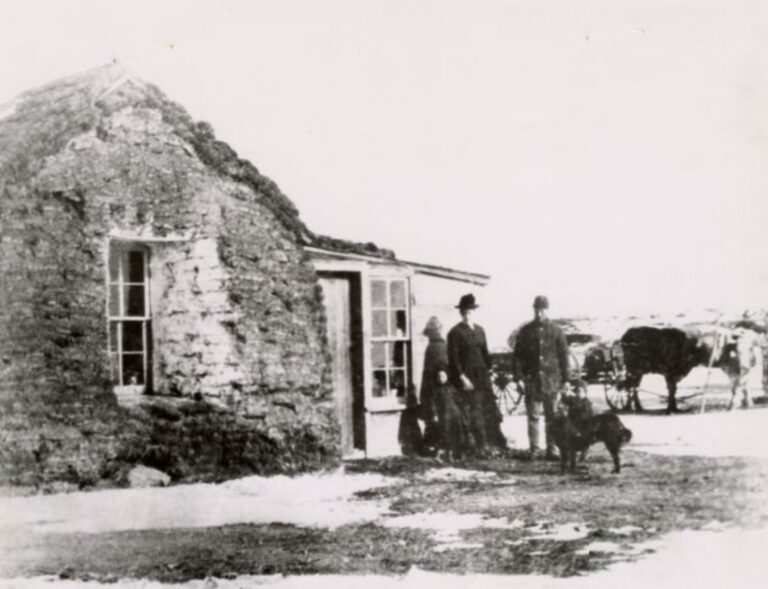 Old stone hut with a rounded thatched roof, a doorway, and people with a horse-drawn cart nearby.