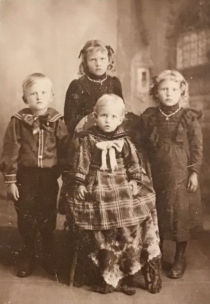 Group portrait of four young children in old-fashioned clothing posing together.
