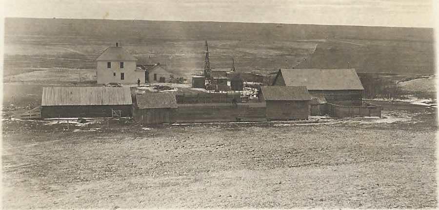 Historic wooden buildings clustered together in a barren landscape, likely a mining camp or frontier settlement.